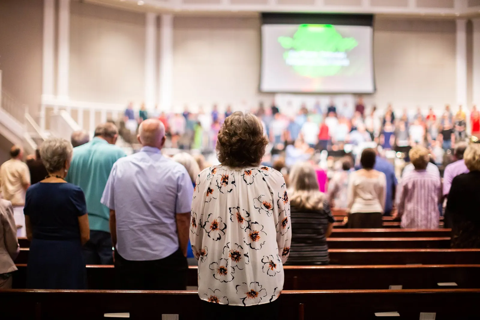 A congregation standing during worship, facing the stage and a large projection screen
