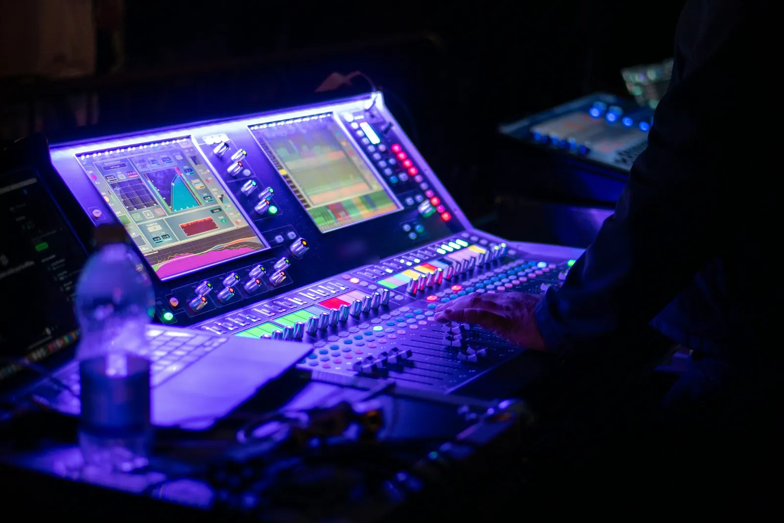 A hand on a lit mixing console in a dark tech booth